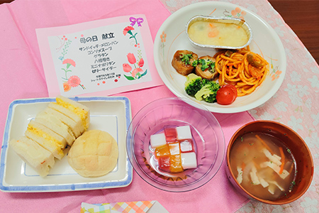 施設の食事風景。サンドイッチ、スパゲッティ、野菜、汁物が盛り付けられた給食